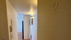 Un corridoio con pavimento in legno, una porta con la scritta '2', un punto luce a parete e un telefono appeso al muro.