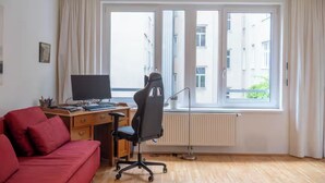 Et værelse med en rød sofa, et skrivebord med en computer og et vindue med gardiner.