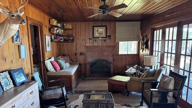 Interior rústico de cabaña con chimenea, paredes de madera, un sofá, un sillón y una decoración con cabeza de venado.