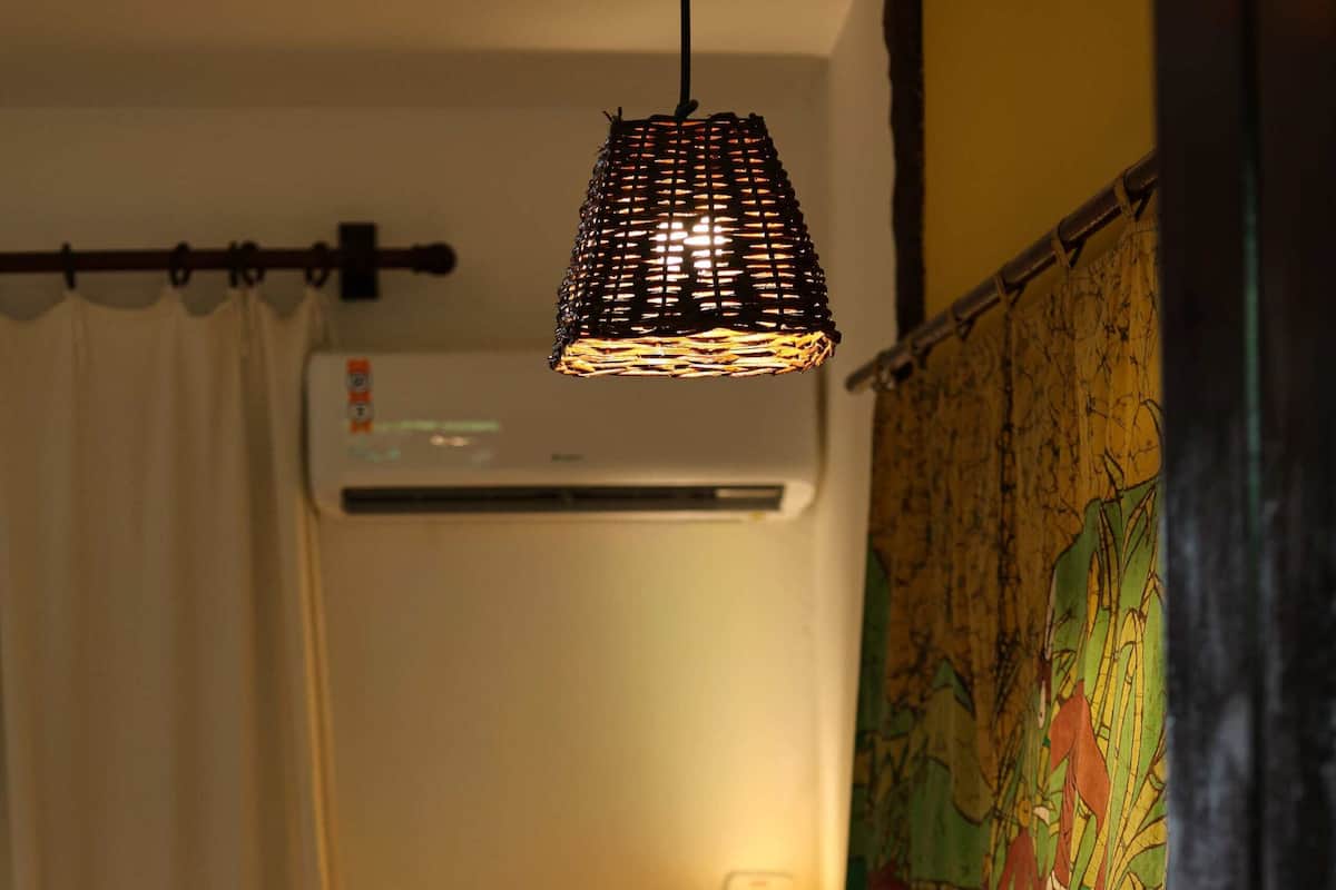 A bedroom with a bed, a hanging light fixture, a wall-mounted air conditioner, and a tapestry.