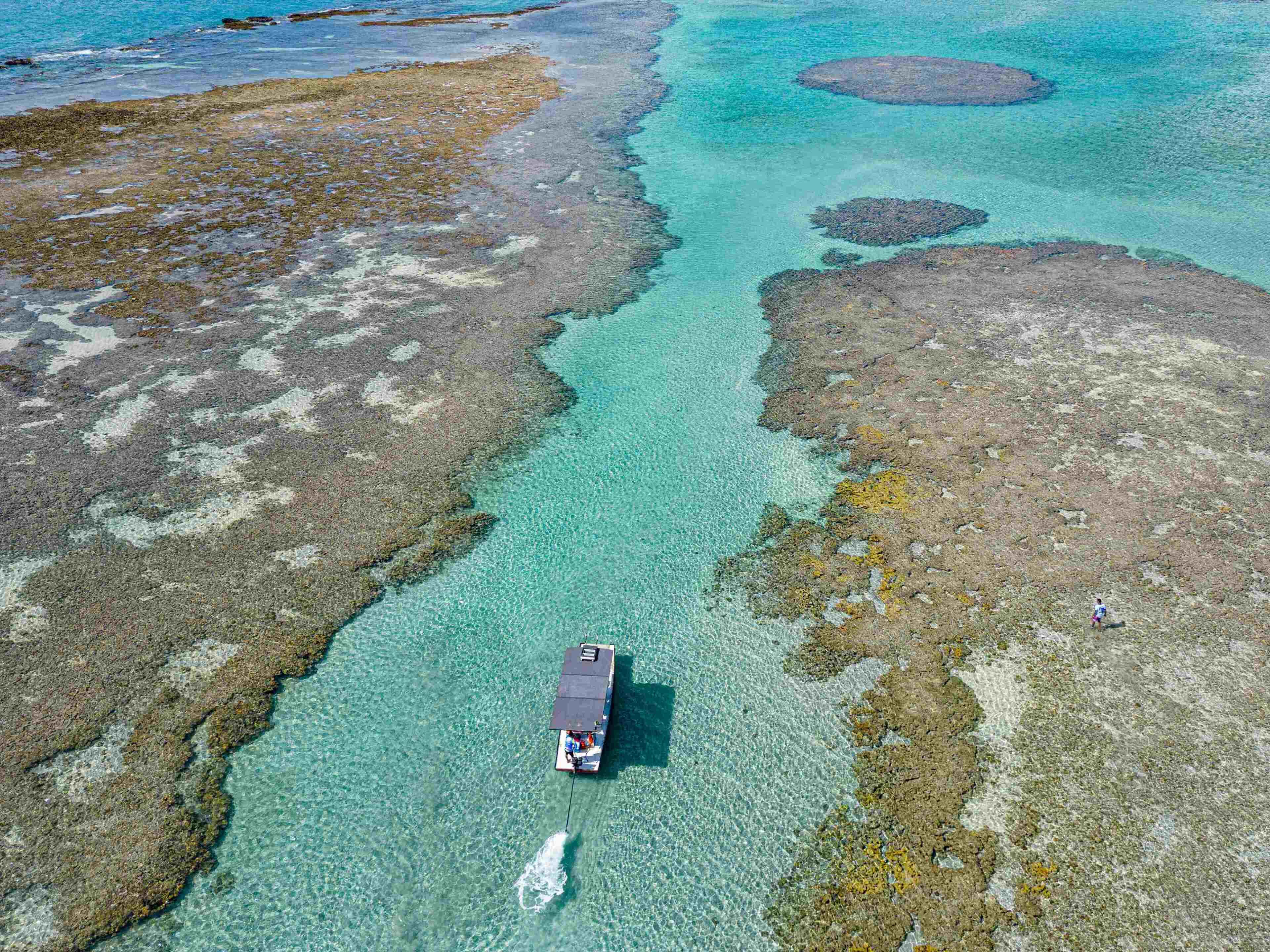 An aerial view of a boat on clear turquoise waters with rocky terrain.
