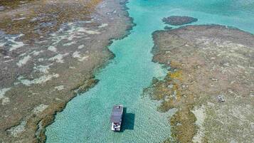 An aerial view of a boat on clear turquoise waters with rocky terrain.