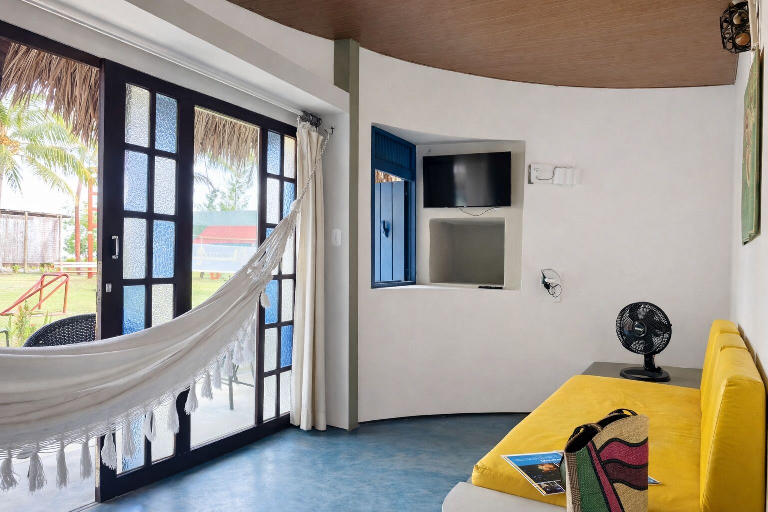 Ein Zimmer mit einer Hängematte, einem gelben Sofa, einem Fernseher und einem Ventilator.