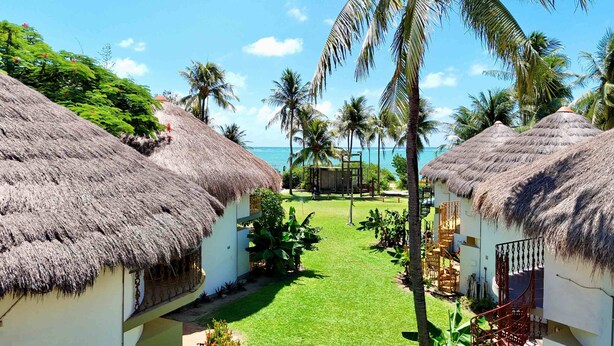 A resort with thatched-roof cottages, a well-maintained lawn, and a view of the ocean.
