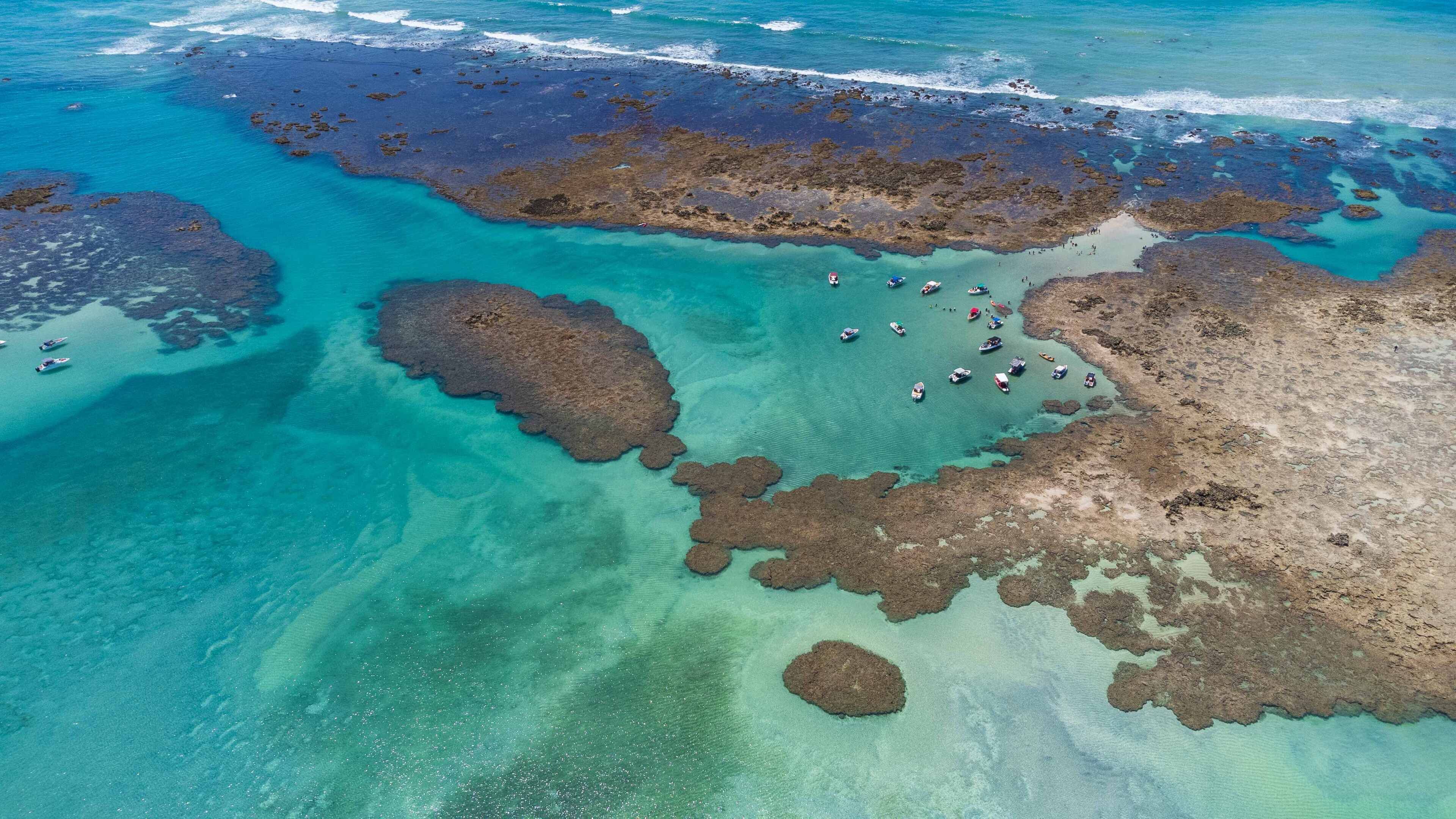 Eine Luftaufnahme einer Küstenlandschaft mit klarem türkisblauem Wasser, Felsformationen und mehreren Booten, die in der Nähe des Ufers vor Anker liegen.