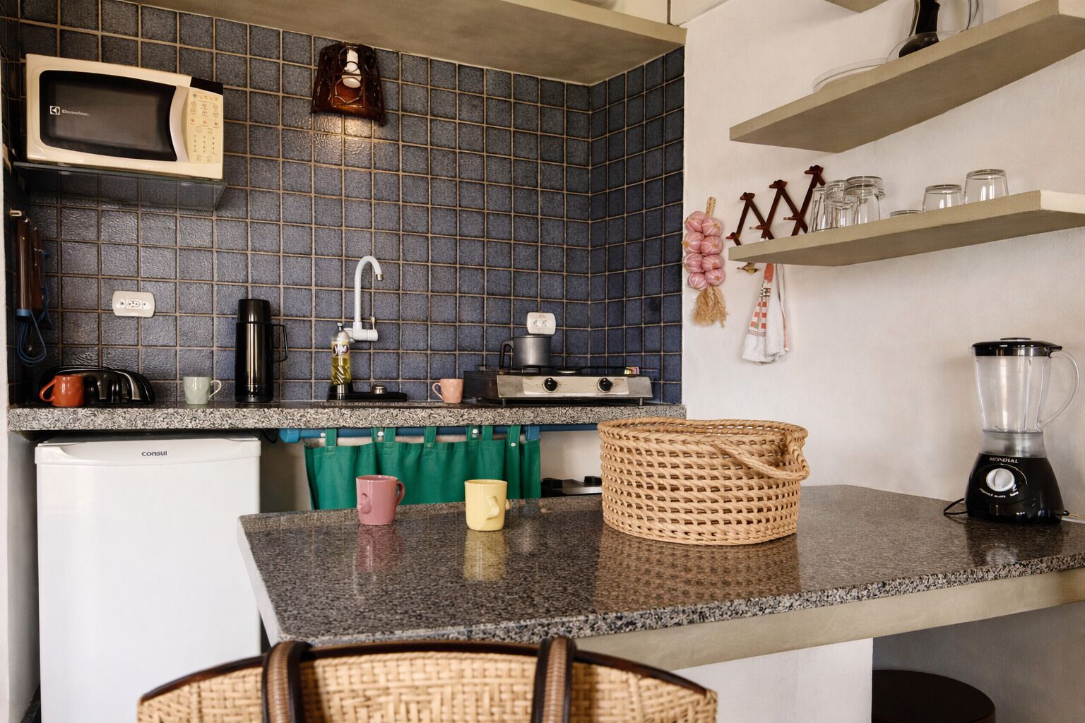 A kitchen with a microwave, coffee maker, kettle, and a blender on the counter. There are hanging kitchen towels and a basket on the counter.