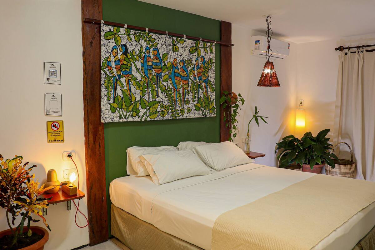 A bed with white linens, a green wall, a mosaic artwork, a hanging lamp, and a potted plant.