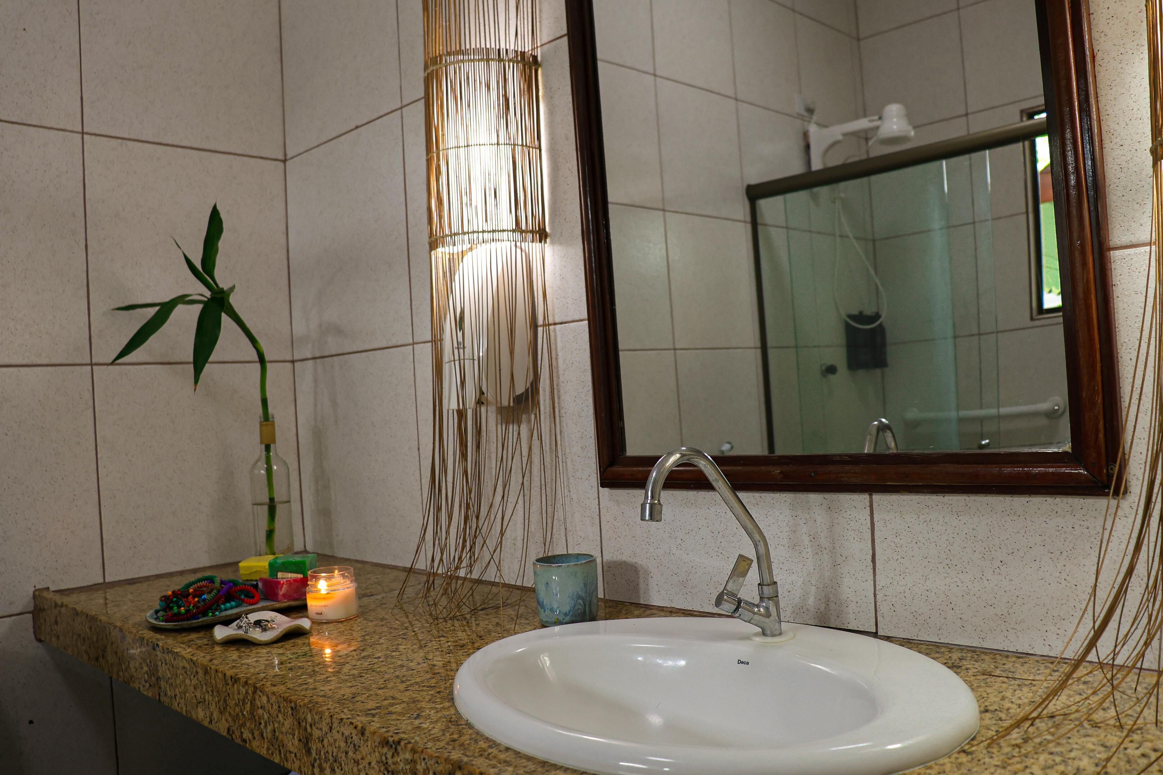 Un baño con lavamanos, espejo y una planta de bambú.