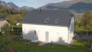 A white building with a sloped roof, surrounded by a grassy area with flowers and a view of mountains in the background. - Mountain house 8 persons 4 épis with Sauna (Arcizans-Avant)
