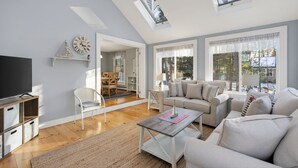 A spacious living room with a high ceiling, a television, a sofa, and a coffee table. - Walk to Beach&Town! 4 Bedrooms|Riverfront|Pet Friendly|Arcade game (Kennebunk)