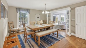 A dining area with a wooden table, chairs, and a bench. There is a window with blinds, a chandelier, and a view of the outdoors. - Walk to Beach&Town! 4 Bedrooms|Riverfront|Pet Friendly|Arcade game (Kennebunk)