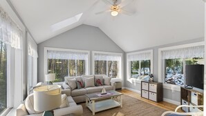 A spacious living room with a high ceiling, large windows, a sofa set, a coffee table, and a television. - Walk to Beach&Town! 4 Bedrooms|Riverfront|Pet Friendly|Arcade game (Kennebunk)