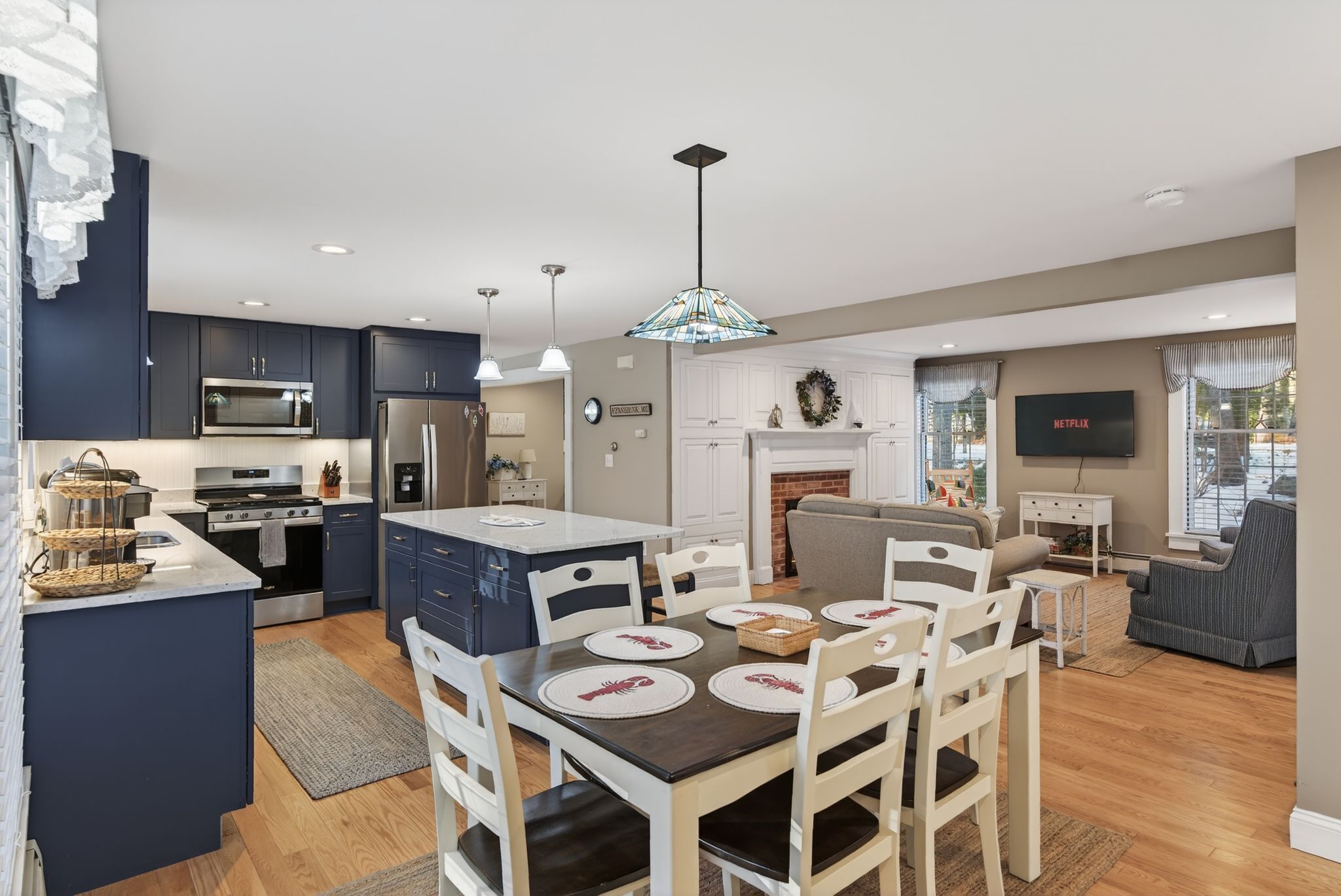A modern kitchen with dark cabinets, a central island, and a dining area with white chairs and a wooden table.