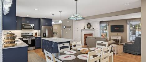 A modern kitchen with dark cabinets, a central island, and a dining area with white chairs and a wooden table.