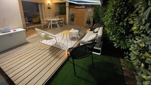 Un patio exterior con terraza de madera, una mesa redonda con sillas, un sofá y una pequeña mesa con una vela.