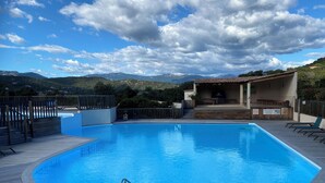 Una piscina con cubierta de madera, un área de estar techada y un paisaje montañoso de fondo.