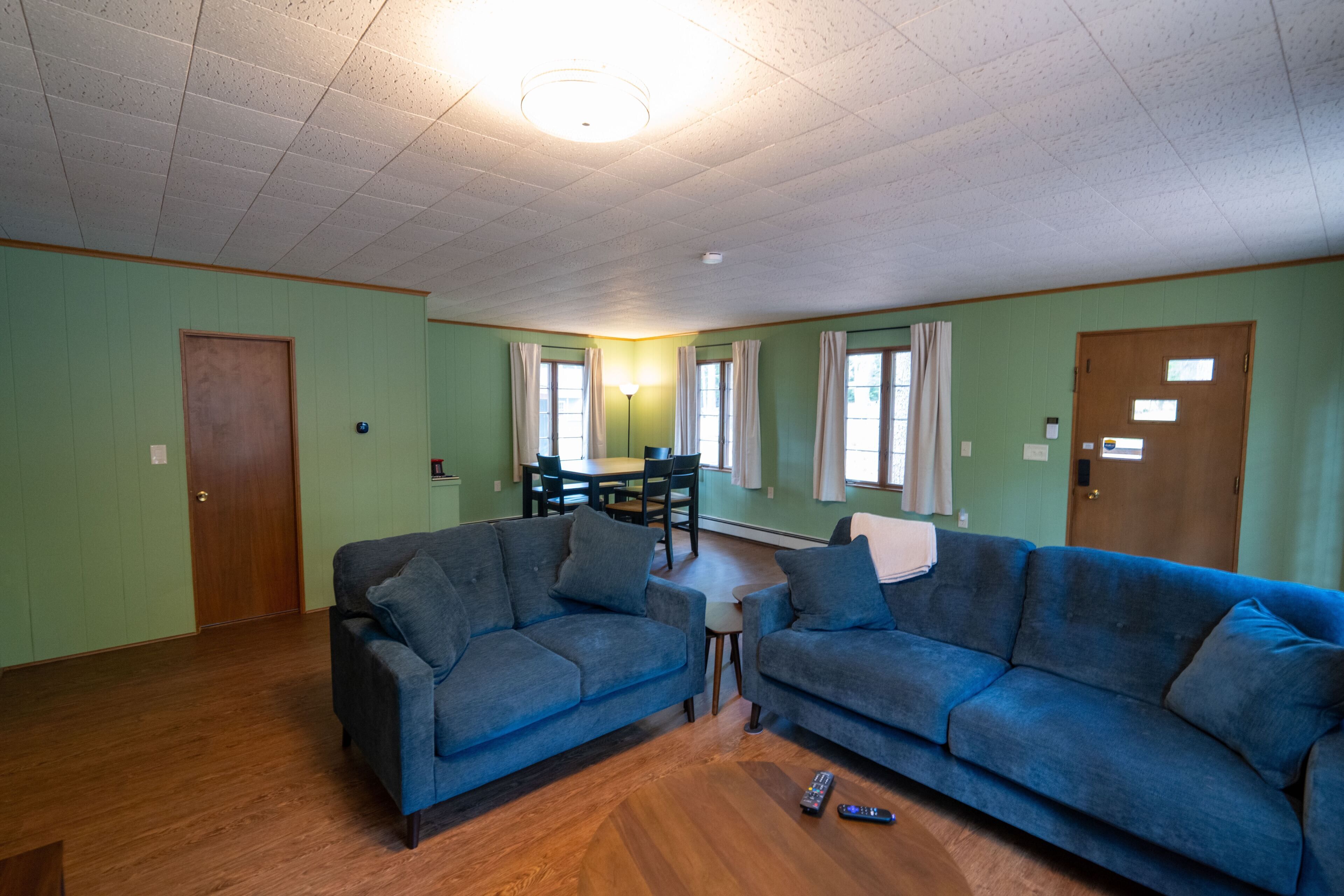 En stue med to blå sofaer, trægulv, et spisebord med stole og en loftlampe.