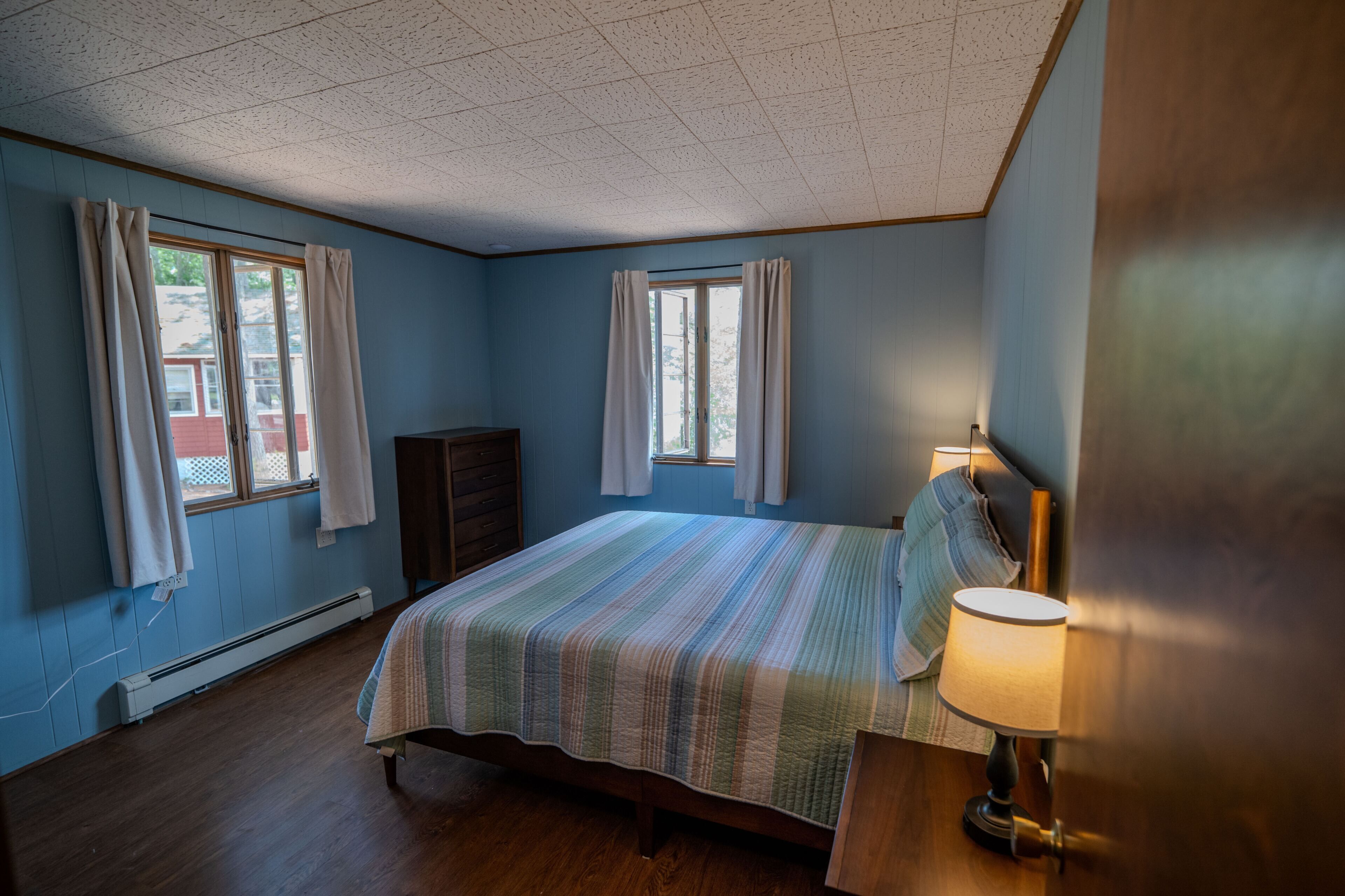 A bedroom with a bed, a nightstand, a lamp, and a window.