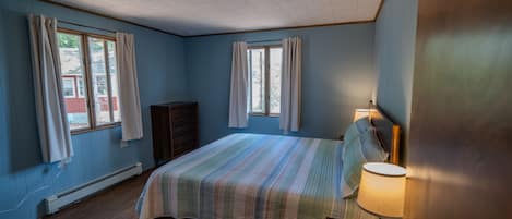 A bedroom with a bed, a nightstand, a lamp, and a window.