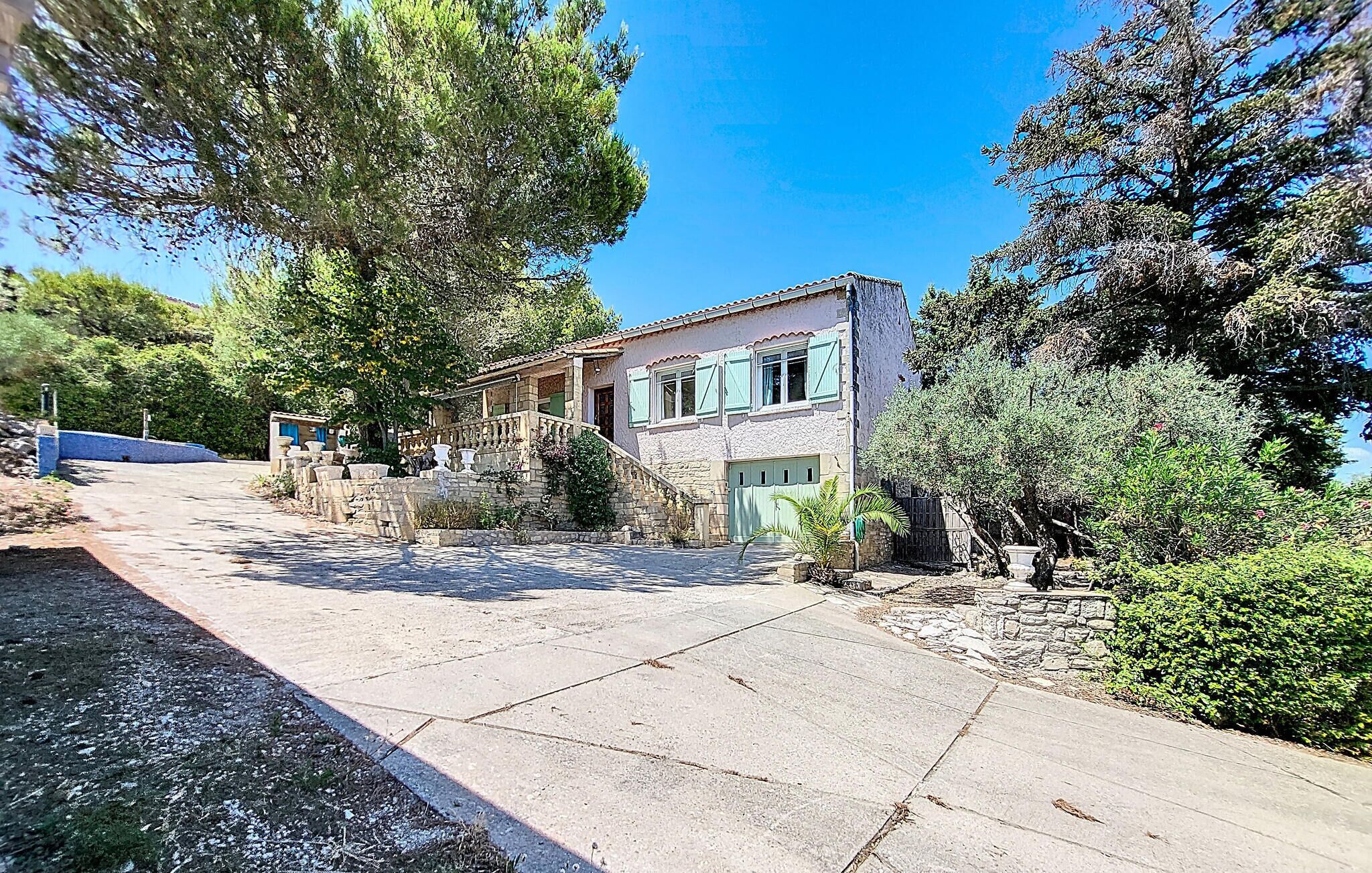 A stone house with a tiled roof, a front porch, and a garden with various plants and trees.