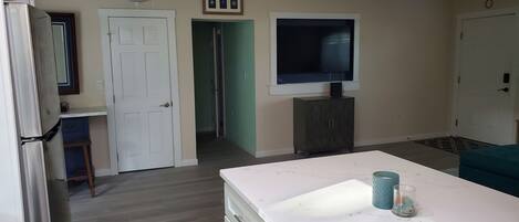 Una habitación con encimera de mármol blanco, un televisor montado en la pared, un ventilador de techo y una puerta que da a otra habitación.