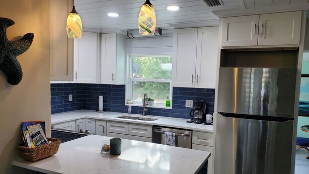 Een moderne keuken met witte kasten, een roestvrijstalen koelkast en hangende lampen.