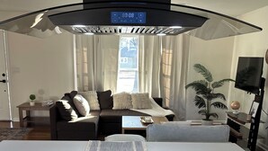 Cozinha moderna com fogão embutido, relógio digital e área de refeições com sofá e mesa de centro.