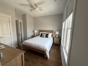 Un dormitorio con una cama de madera, dos mesitas de noche con lámparas, un ventilador de techo y una puerta.