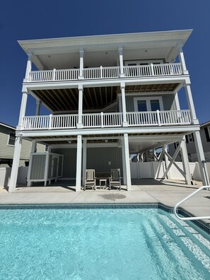 A two-story house with a balcony, a pool, and a covered patio area. - New Build! 3rd Row, Ocean Views, Elevator, Large Private Pool, 5 BR, 5.5 BA! (Ocean Isle Beach)