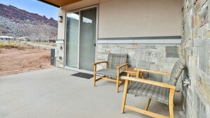 Eine überdachte Terrasse mit zwei Korbstühlen und einem Tisch, einer Steinmauer und Blick auf eine gebirgige Landschaft.