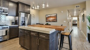 A modern kitchen with dark cabinetry, stainless steel appliances, a wooden island, and pendant lighting. - C2-C3 Combo - Moab Sage Creek Resort - Heated Pool (Moab)