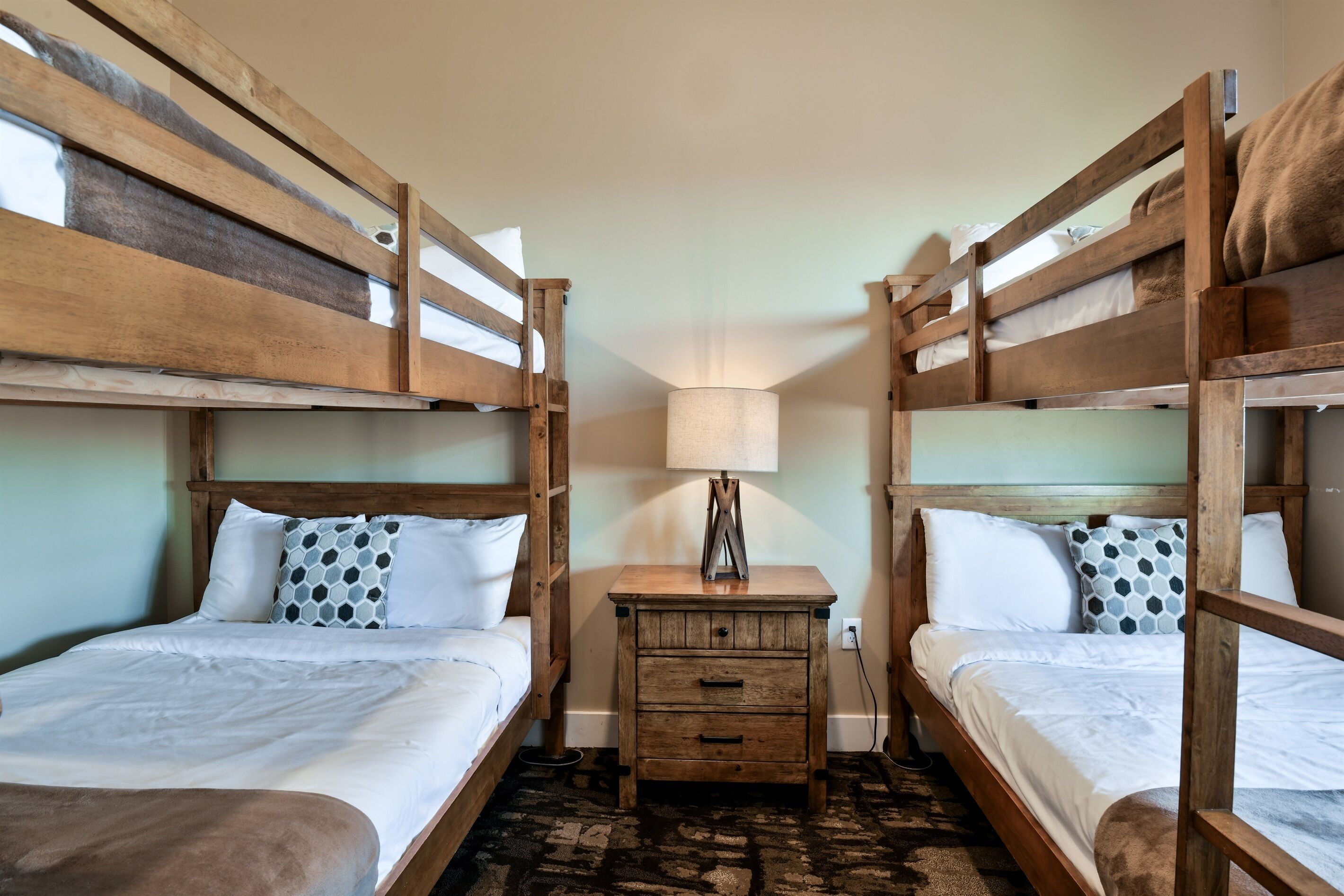 Une chambre avec un lit superposé, deux lits, une table de chevet avec une lampe et un tapis à motifs.