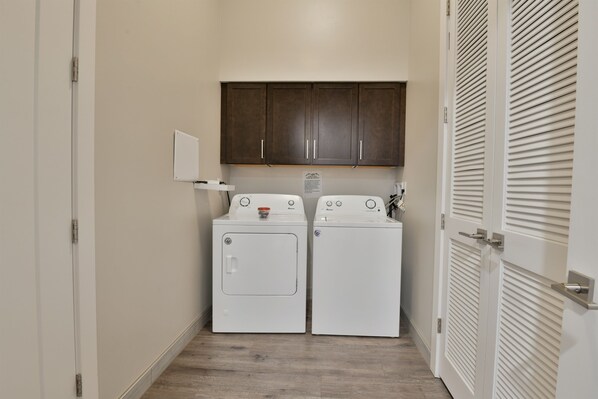 A laundry room with two white front-loading washers and dryers, wooden cabinets above, and a white door with louvered panels.