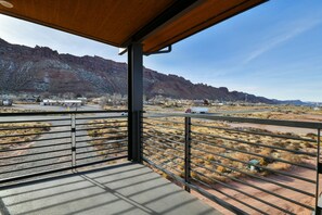 A balcony with a view of a mountainous landscape, a paved area, and a building in the distance.