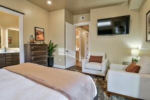A hotel room with a bed, two white armchairs, a TV, a dresser, and a plant. - C9 and C12 Combo - Sage Creek - Elevated Pool View (Moab)