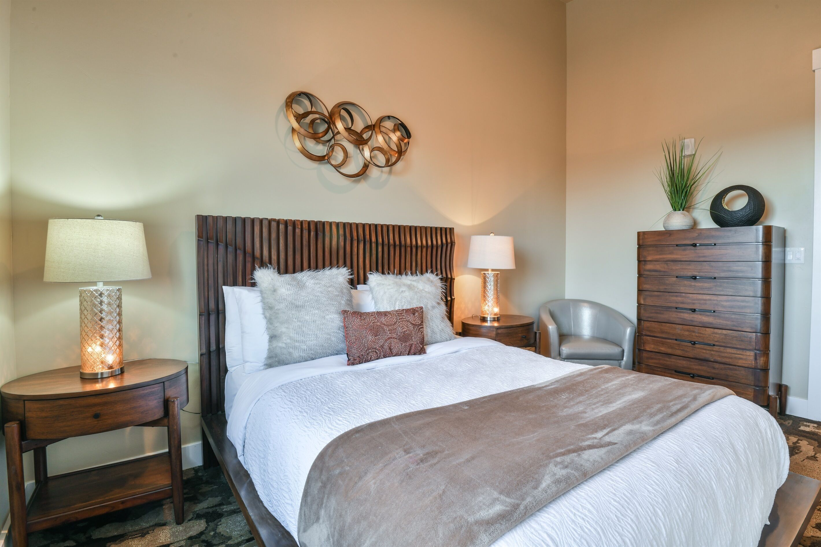 Une chambre d’hôtel bien aménagée, avec un grand lit, deux tables de chevet avec des lampes, une commode en bois et un élément décoratif mural.