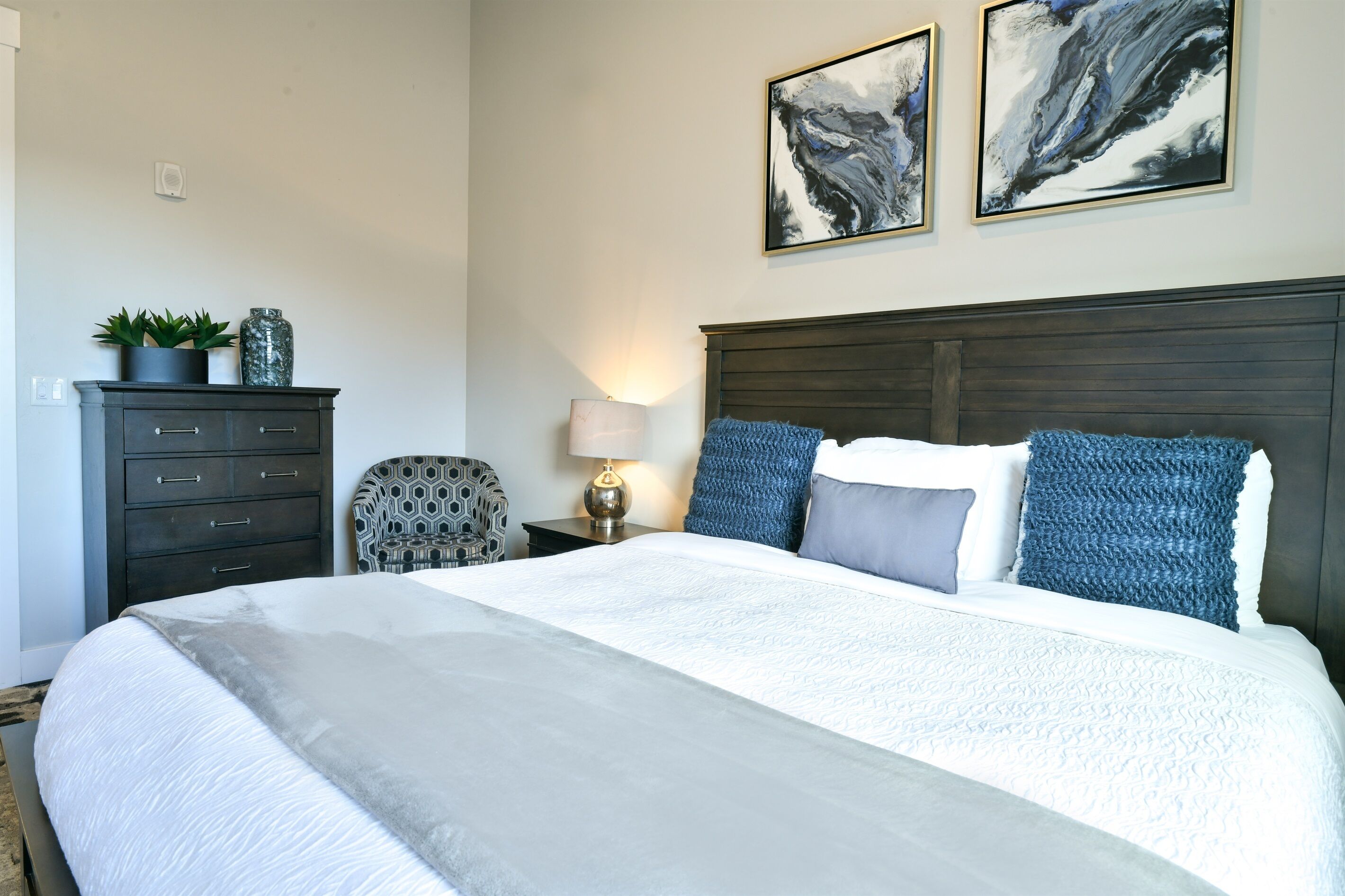 A neatly arranged bedroom with a large bed, a dark wooden headboard, and two abstract paintings on the wall.