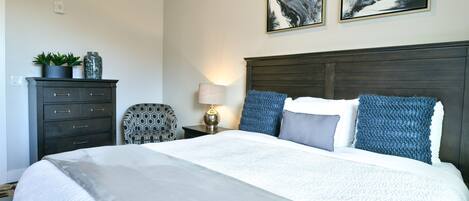 A neatly arranged bedroom with a large bed, a dark wooden headboard, and two abstract paintings on the wall.