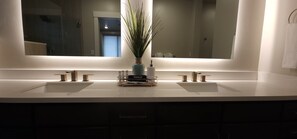 Een moderne badkamer met een grote spiegel, twee wasbakken en een decoratieve plant.