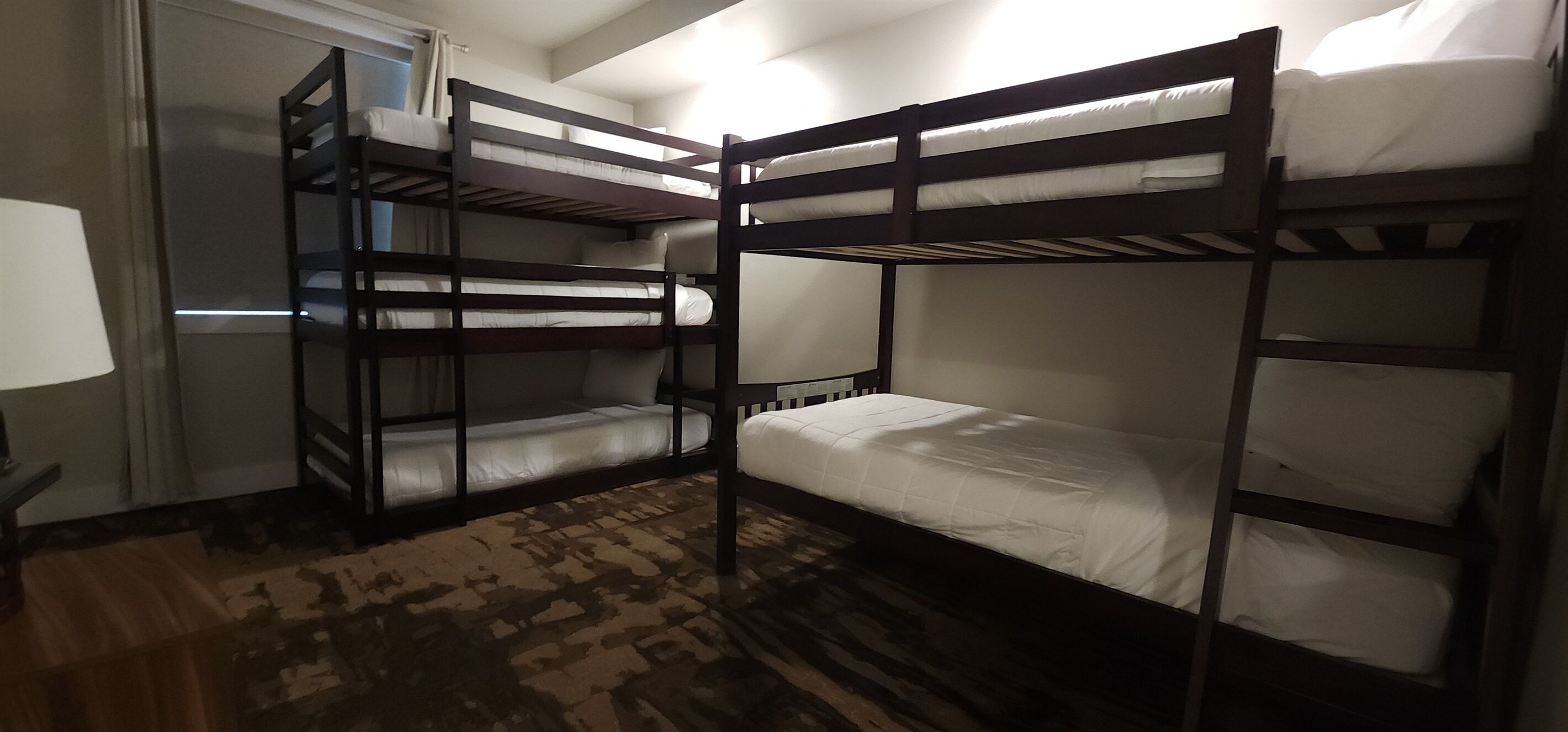Habitación con literas, una alfombra estampada, una lámpara y una ventana con cortinas.