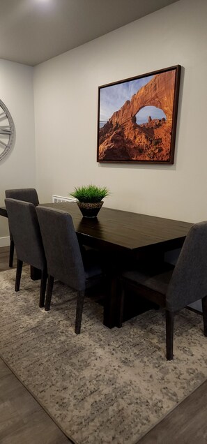 A dining area with a dark wooden table, four grey upholstered chairs, a potted plant, and a framed landscape painting on the wall. - D1 and D4 Combo Unit - Sage Creek Resort Moab (Moab)