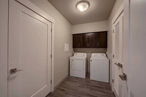 A laundry room with two washing machines, a cabinet above them, and a door on the left. - D1 and D4 Combo Unit - Sage Creek Resort Moab (Moab)