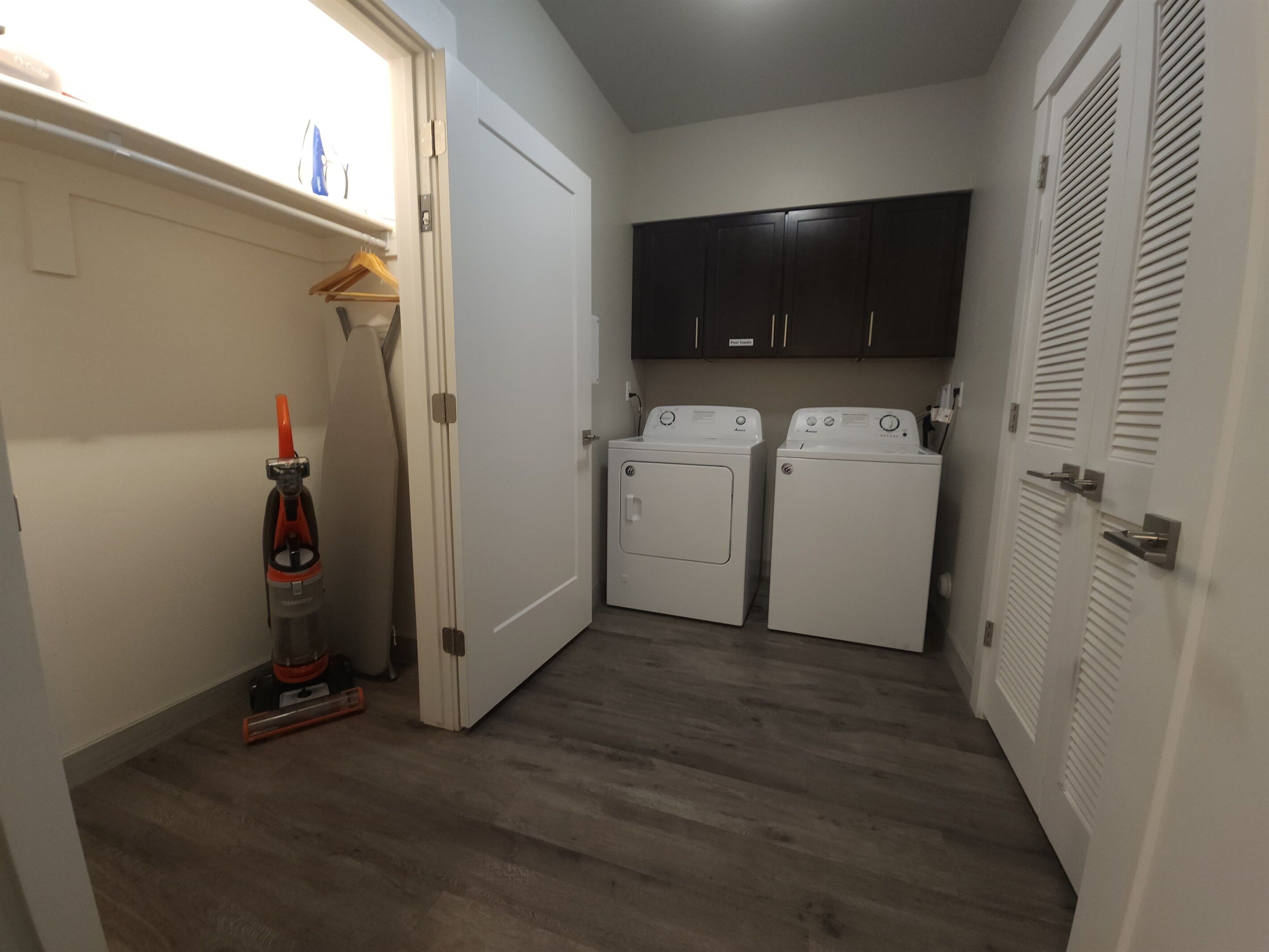 A laundry room with two washing machines, a vacuum cleaner, and a wooden floor.