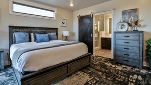 Ein Schlafzimmer mit einem großen Bett, einem Deckenventilator, einer Schiebetür zu einem Badezimmer und einer Kommode mit Schubladen.
