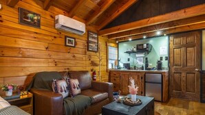 A cozy cabin interior with a leather sofa, a small table, a kitchen area, and wooden walls.