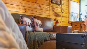 A cozy cabin interior with a leather sofa, a blanket, and a vintage suitcase.