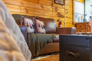A cozy cabin interior with a leather sofa, a blanket, and a vintage suitcase. - Romantic Getaway for Two 16 mi from Hocking Hills with hot tub, grill&twin ponds (McArthur)
