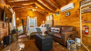 A cabin interior with a bed, a sofa, a small table, and a fireplace.