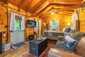 A cozy cabin interior with a wooden ceiling, a bed, a sofa, a television, and a fireplace. - Hocking Hills Couples Cabin with private hot tub (McArthur)