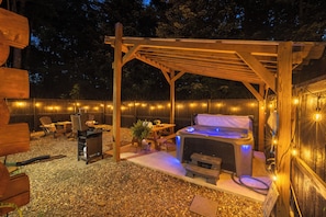 An outdoor patio area with a wooden pergola, a barbecue grill, a hot tub, and string lights. - Hocking Hills Couples Cabin with private hot tub (McArthur)